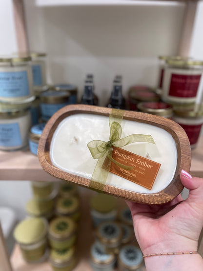 Hand holding a scented candle labeled 'Pumpkin Ember' with a blurred store shelf in the background.